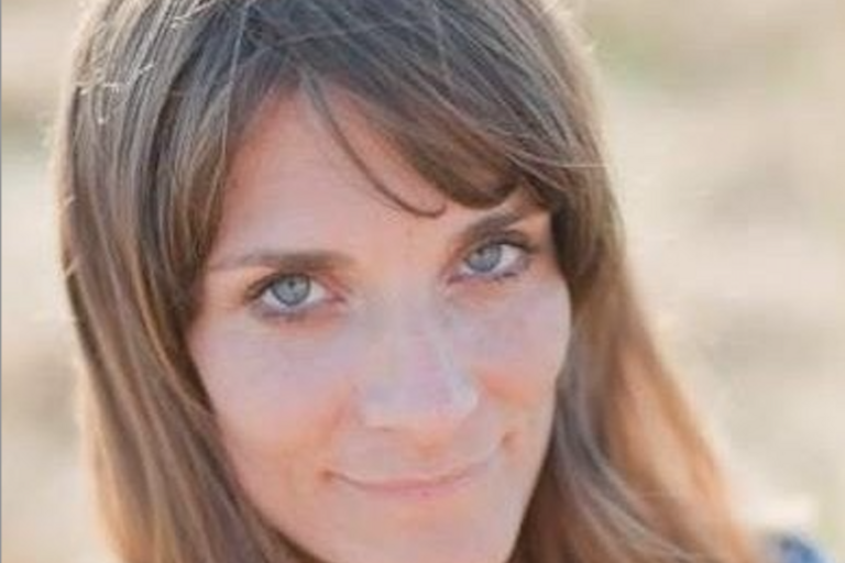 Close-up of a person with blue eyes and light brown hair, smiling slightly.