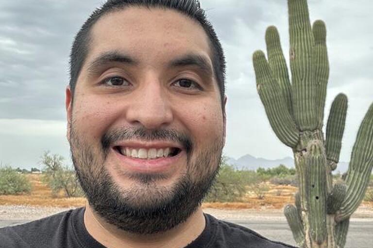 Man with short dark hair standing in front of cactus