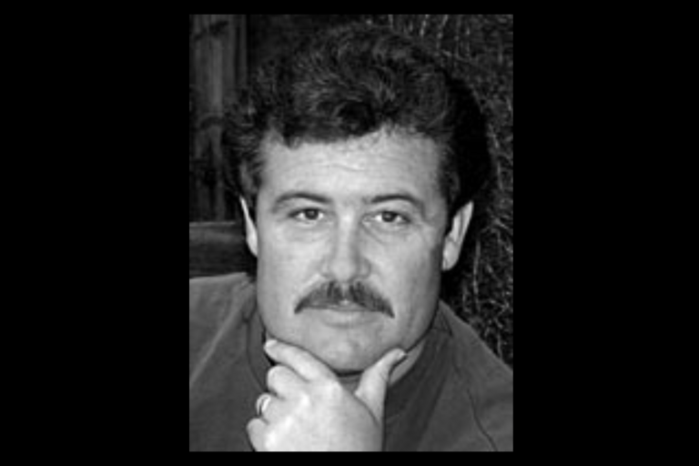 Black-and-white portrait of a middle-aged man with a mustache, resting his chin on his hand.