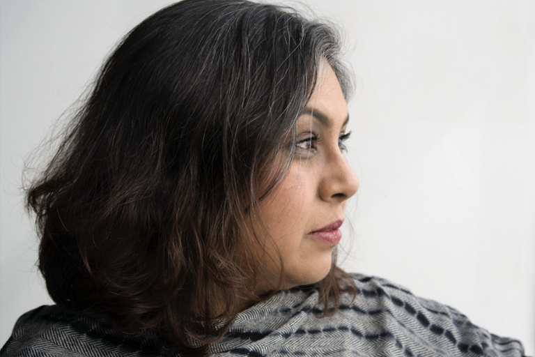 Close-up profile of a person with dark, wavy hair with gray strands, facing right.