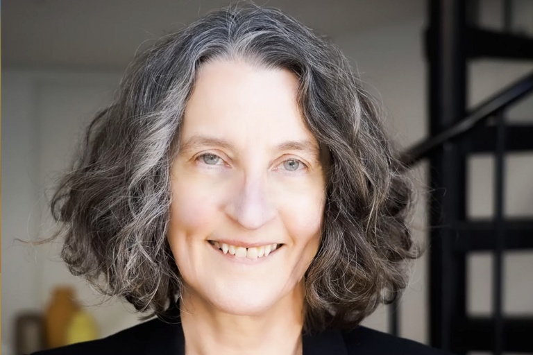 A smiling person with shoulder-length grey hair.