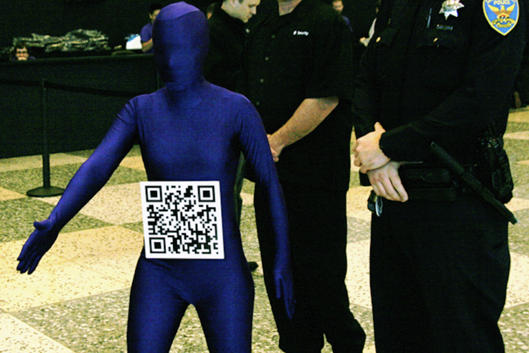 Person in a blue full-body suit with a QR code on their abdomen, standing next to security personnel and a police officer indoors on a tiled floor.