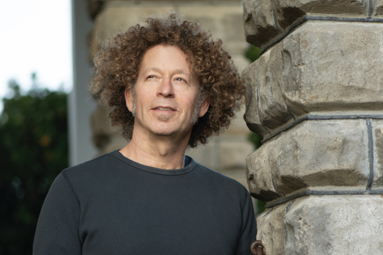Person with curly hair standing outdoors next to a stone structure.