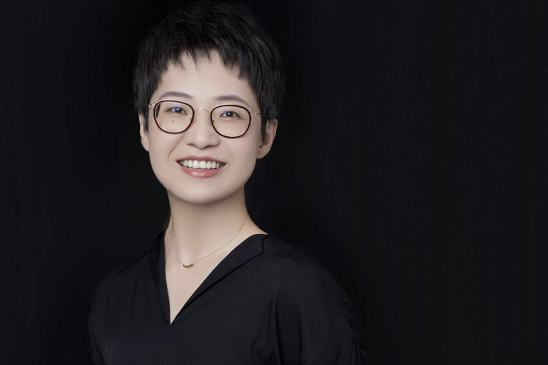 Portrait of a person with short, dark hair, glasses, and a black top.