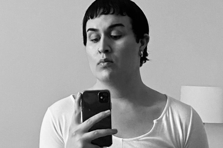 Person taking a selfie with a phone, wearing a light-colored top, in a grayscale image.