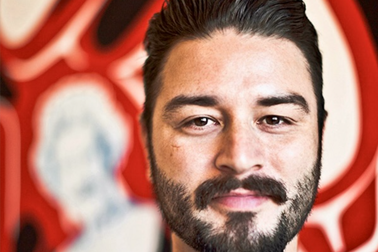 Close-up of a man with a beard against a colorful, abstract background.