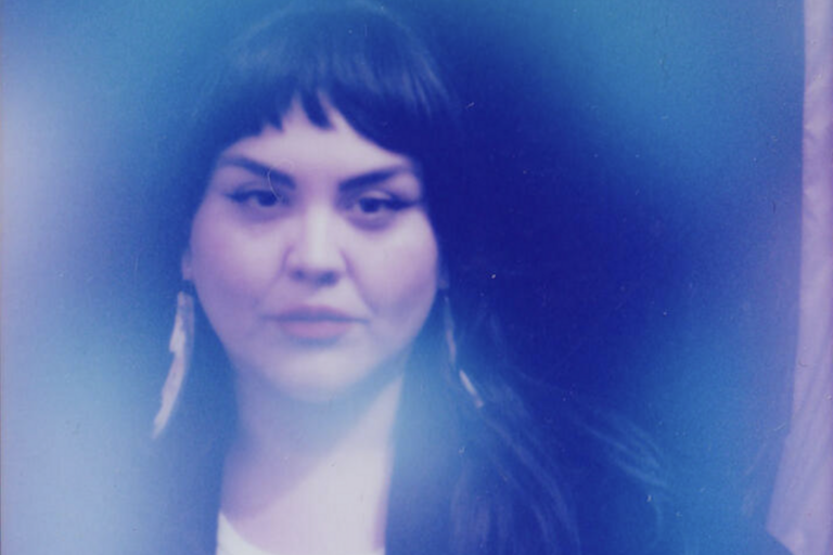 A person with dark hair and earrings enveloped in a blue haze.