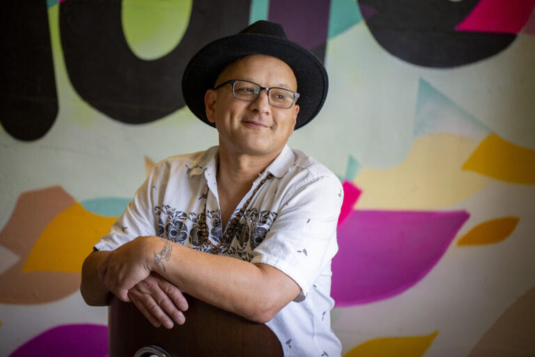 Person leaning on a wooden chair with a colorful mural in the background.