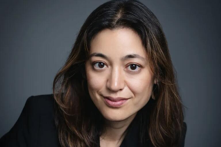 Headshot of a woman with long brown hair and a slight smile against a gray background.