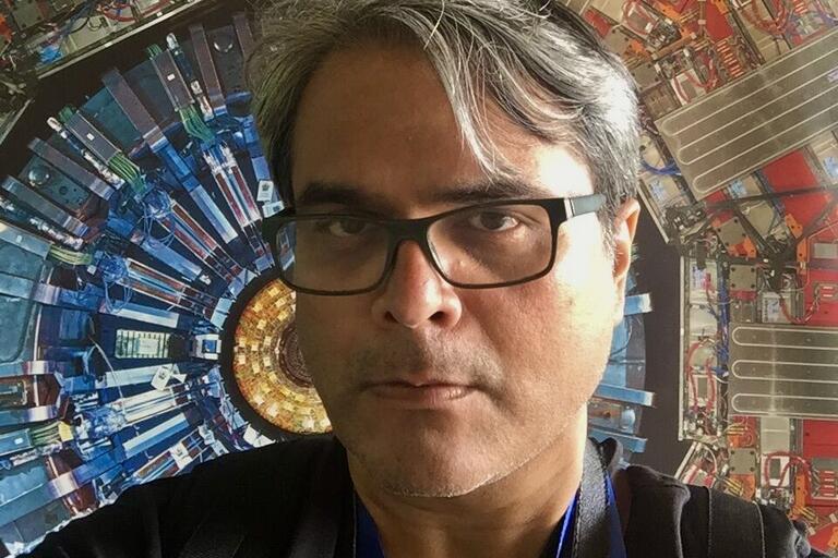 Man with glasses in front of complex circular machinery.