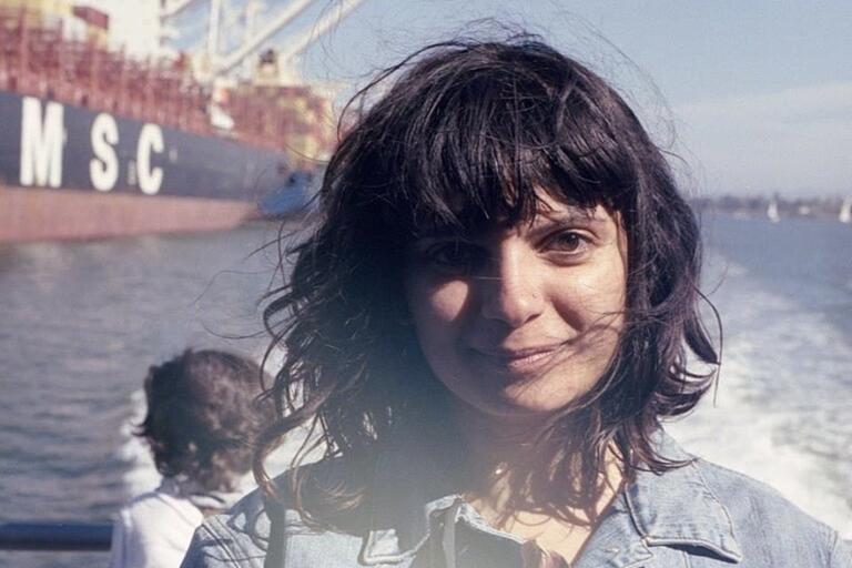 Woman in a denim jacket standing in front of a cargo ship with the letters "MSC" on its side.