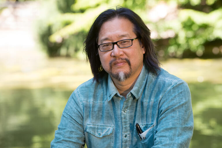 A person wearing glasses and a light blue shirt in an outdoor setting.