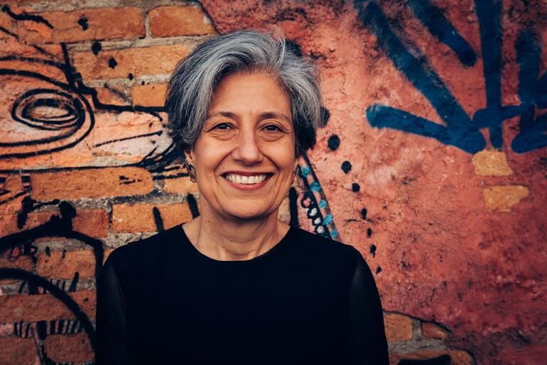 Smiling woman with short, gray hair against a graffiti-covered brick wall.