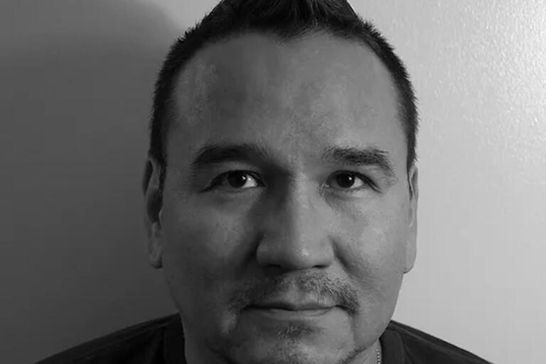 Black-and-white photo of a person with short, spiked hair, looking directly at the camera.