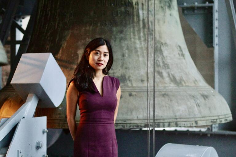 Woman in a purple dress standing in front of a large weathered bell.