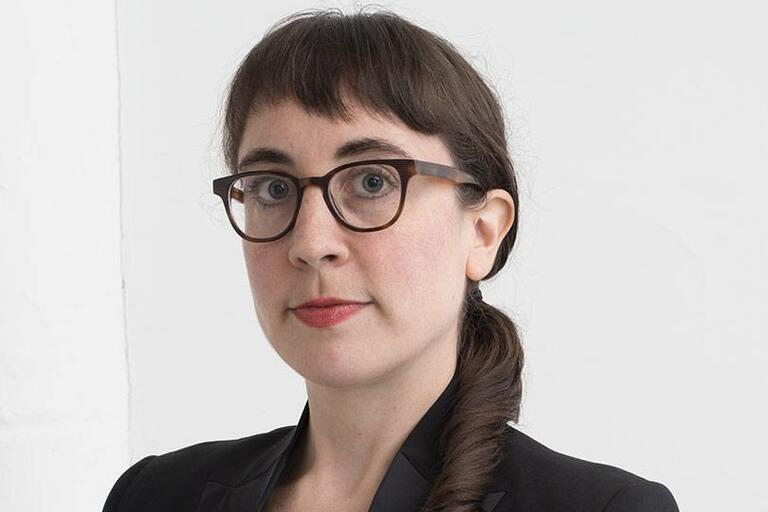Person with long dark hair in a side braid wearing tortoiseshell glasses and a black blazer.