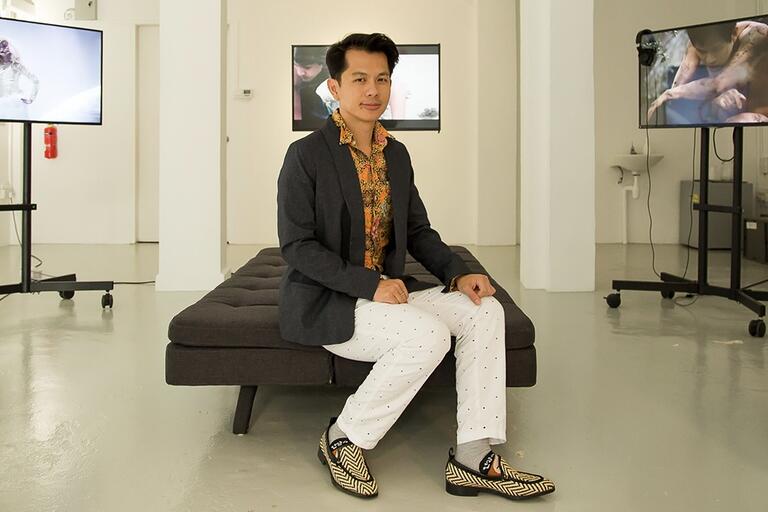 Man sitting on a gray bench in a modern, minimalist gallery space with artwork displayed on TV screens.