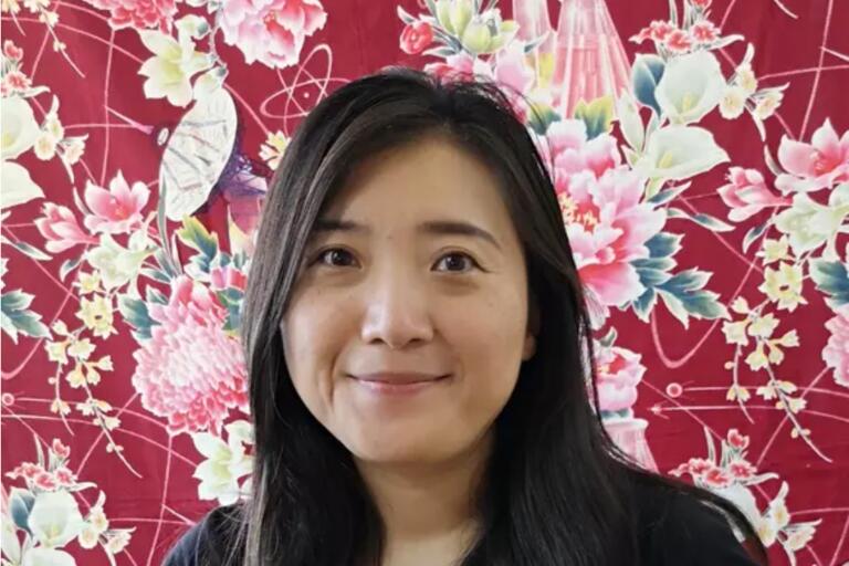A woman with long dark hair smiles in front of a red, floral and science-themed background.