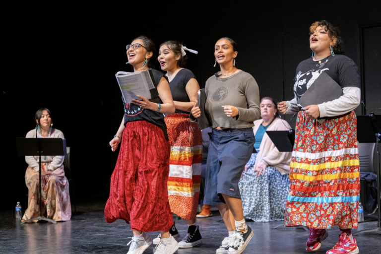 Four young people jog on a stage, some holding scripts in hand