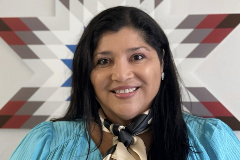  A woman in a blue shirt and scarf, smiling warmly against a neutral background.