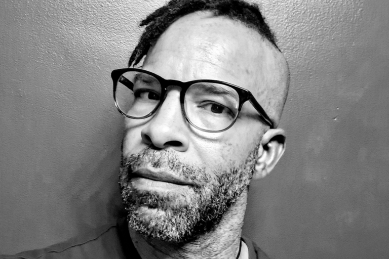 A black and white portrait of a man wearing glasses, showcasing his thoughtful expression and classic style.