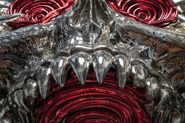 A detailed view of a metal sculpture featuring striking red eyes, showcasing intricate craftsmanship and design.