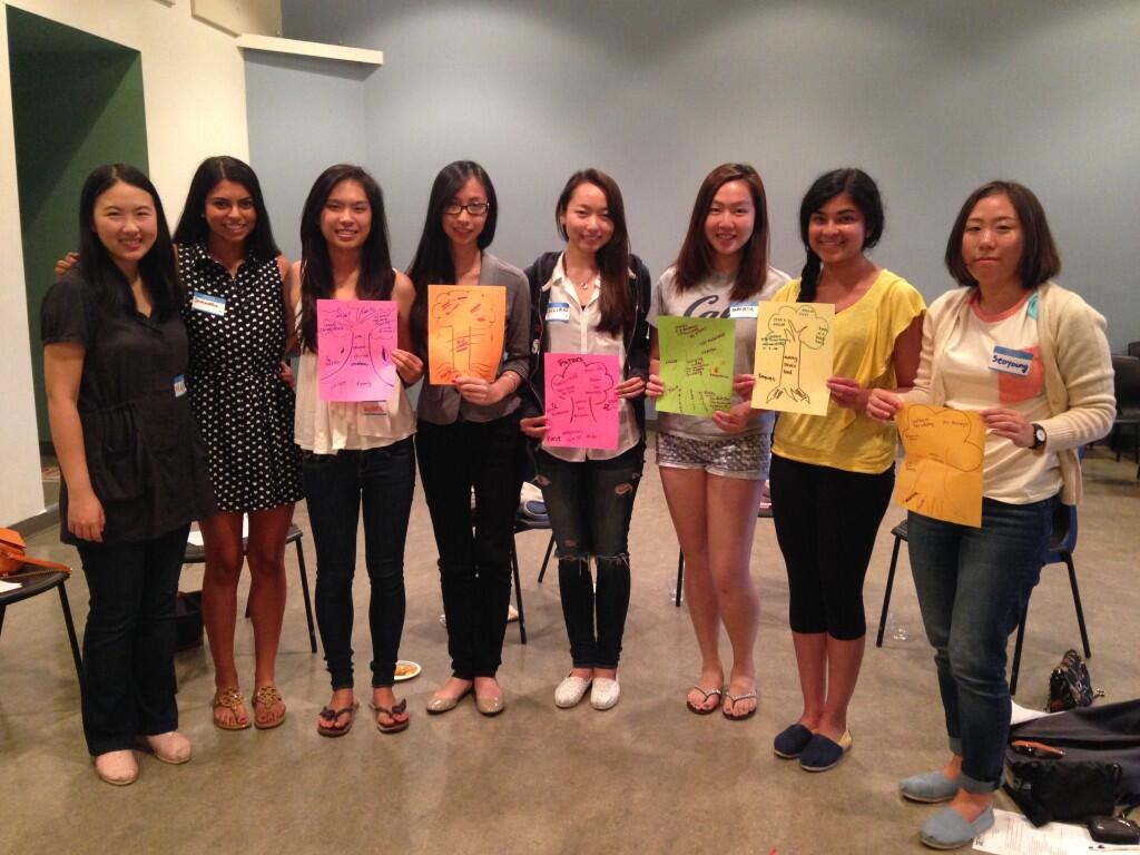 8 women pose for a photo, holding up drawings and smiling