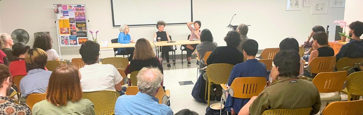 three women speakers at a table in front of an audience