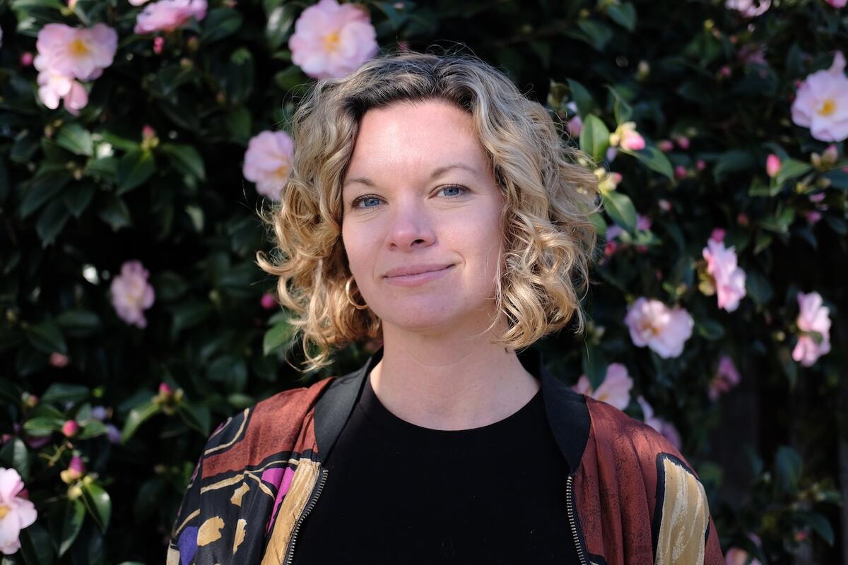 Woman with blonde curly short hair and black outfit against pink roses