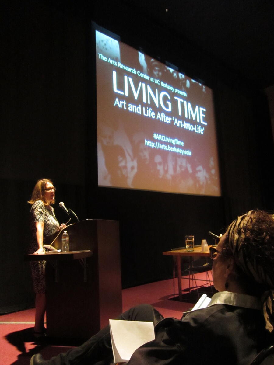 Woman presenting a lectern in front of a screen reading "Living Time"