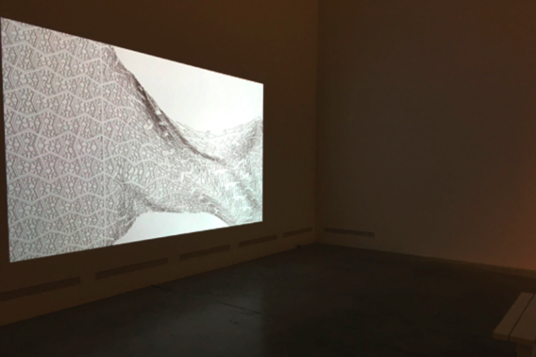 Still of a exhibition where na abstract Black & white video is playing of a pattern melting away