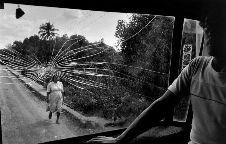 Man standing in shadows in front of cracked windowsheild where a nun walks barefoot