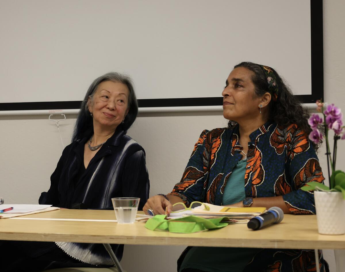 Two women seated at a table, with a projector screen in the background, engaged in conversation.