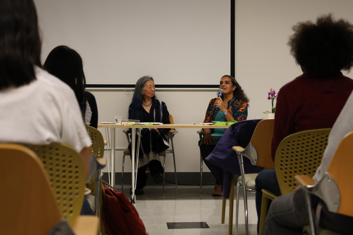 Two people seated in front of an audience during a panel discussion, one holding a microphone.