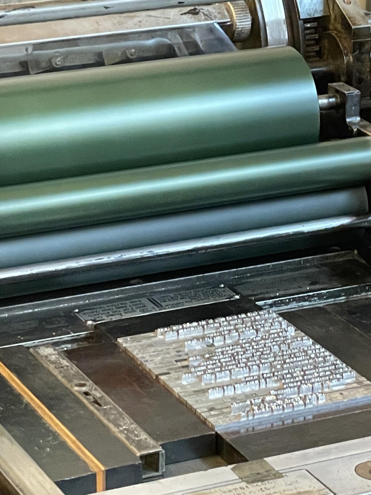 Close-up of a printing press with green rollers and a typeset layout.