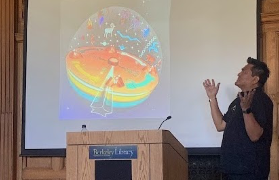 Person presenting at a podium with a colorful illustration projected on a screen behind.