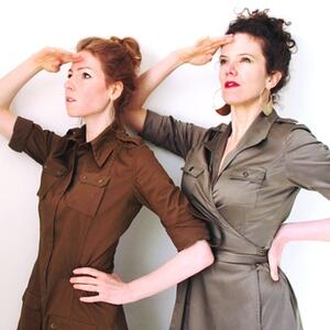 Two people saluting and looking upward against a white background, wearing brown and grayish-green dresses.