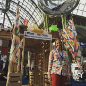 A person stands in front of a wooden booth with colorful flags and a reflective sphere overhead.