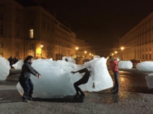 People interacting with large ice blocks on a cobblestone street at night.