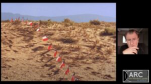 Desert landscape with red and white flags and an inset image of a person next to an "ARC" logo.