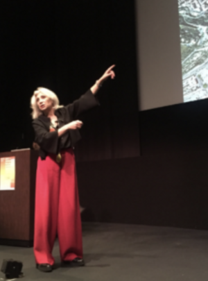 Person on stage pointing at a projected map or graphic.