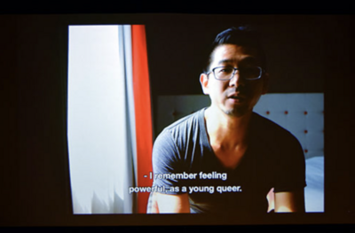 A person speaking in a dimly lit room with a window on the left.