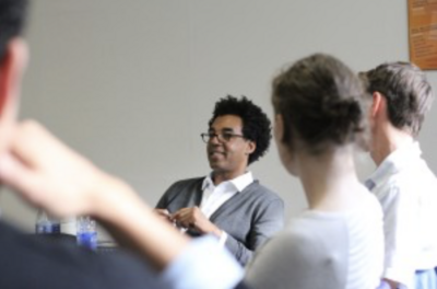 Person with glasses and curly hair engaging with two people in a room.