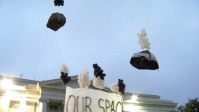 Black and white clusters of balloons attached to packages float above a classical building with a sign reading "OUR SPACE".